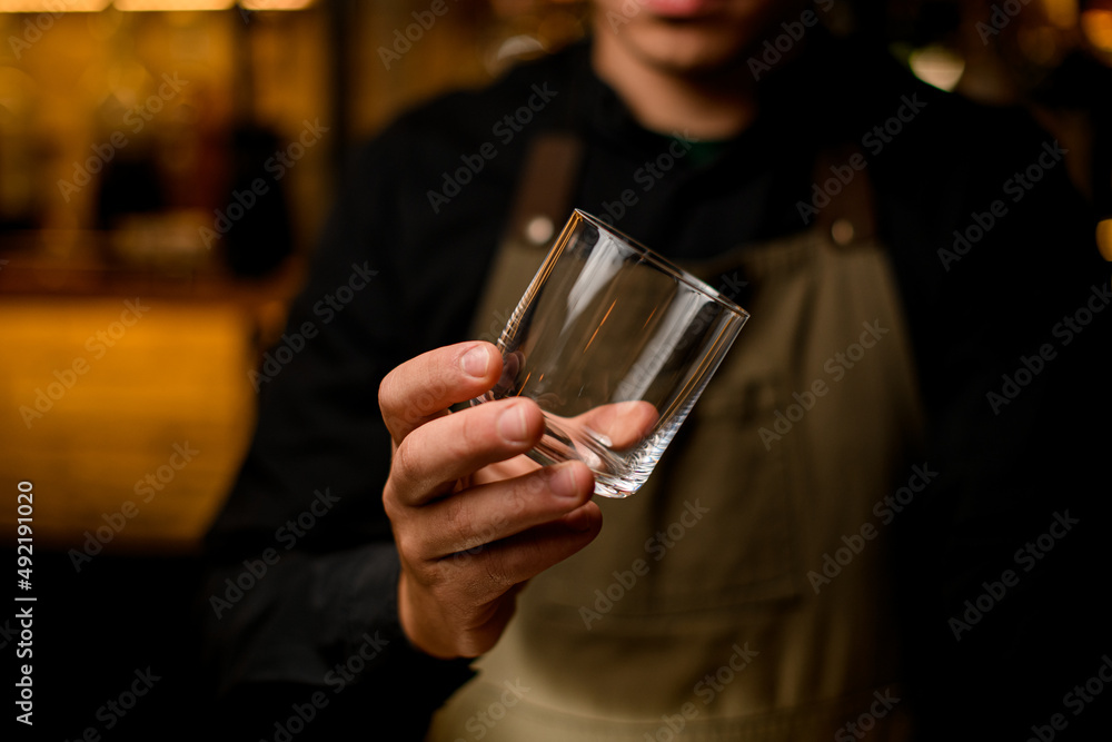 close-up view of empty glass for drink in hand of male bartender
