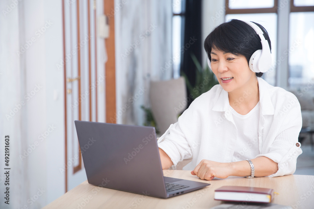 The adorable Asian businesswoman in headphones communicates online sits on a laptop in the office. healthy lifestyle. work from home The adorable Asian businesswoman in headphones communicates online sits on a laptop in the office. healthy lifestyle. work from home