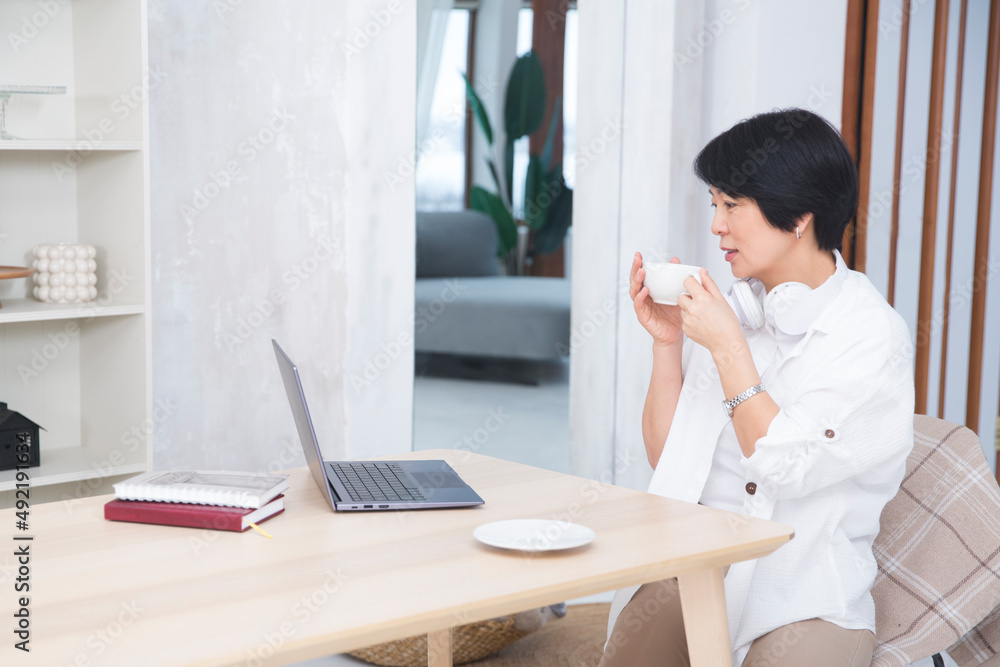 The adorable Asian businesswoman sits on a laptop and drinks tea in the office. rest from work. healthy lifestyle. work from home The adorable Asian businesswoman sits on a laptop and drinks tea in the office. rest from work. healthy lifestyle. work from home