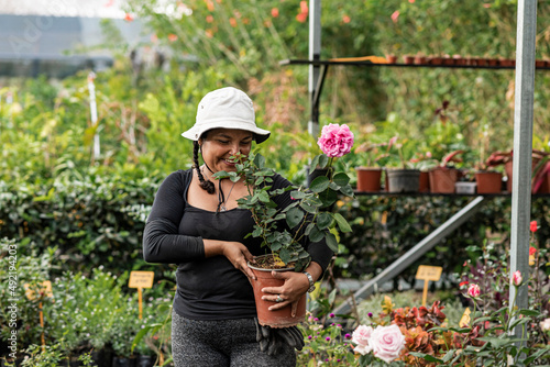 Short, heavy-set Latina woman working in her botanical garden with a hat on her head, very happy.