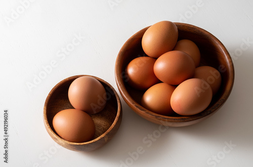 Top view brown eggs in wooden bowl on white table.