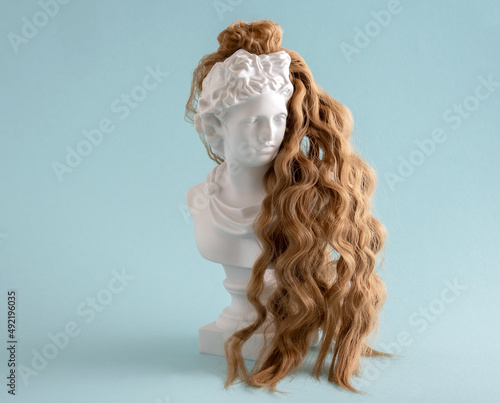 White statuette with long, healthy, well-groomed curly hair on blue background. Hair health and curly hair care concept.