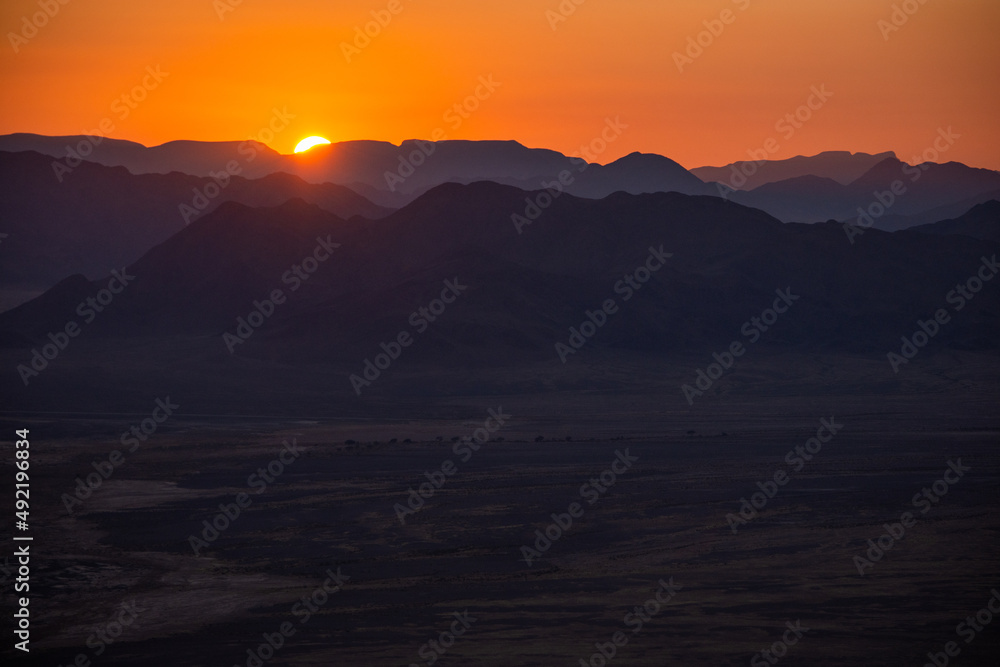 Namibian mountainlandscape seen at sunrise from aerial view with sun just showing and orange sky