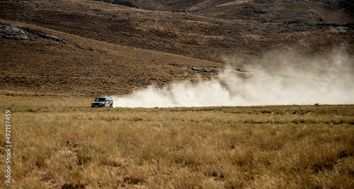 The car drives quickly through the mud with clouds of dust from under the wheels, against the backdrop of the mountains. Rally Dakar. Off-road vehicle rides off-road in the desert. © Vera