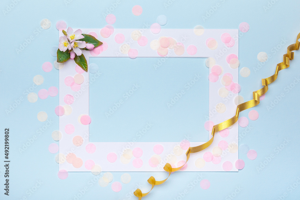 Spring concept with apple bloom on light blue background with copy space. White frame with pastel colored confetti and golden ribbon with copy space, top view.