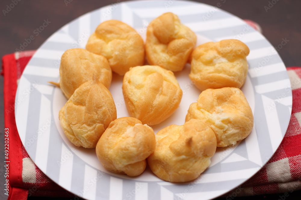 The eclair is placed in a white plate on a wooden table. The eclair is placed in a white plate on a wooden table.