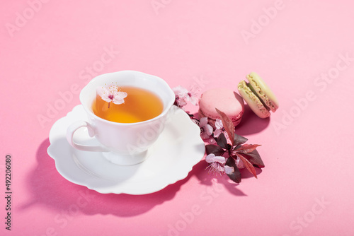 Tea with pink spring cherry blossom served in a porcelain tea cup and a macaron.