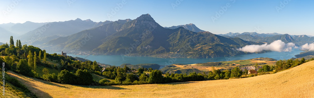 Summer panoramic view of Serre-Poncon Lake with Grand Morgon Peak and Savines-le-Lac village. Hautes-Alpes (Alps). France