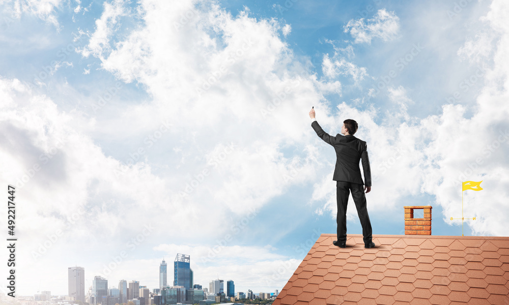 Businessman on house roof touch empty space. Mixed media Businessman on house roof touch empty space. Mixed media