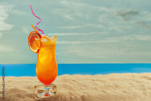 Orange cocktail on the beach. Alcoholic drink with ice, orange on the sand close up. Sunset, sea and sky in the background. Copy space and free space for text near the glass.