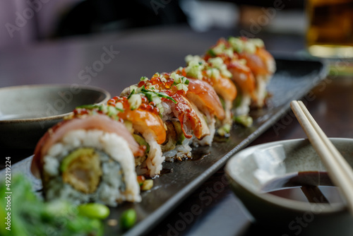Selective focus at Dragon Roll, roll of sushi on top with fresh raw fish on black dish.