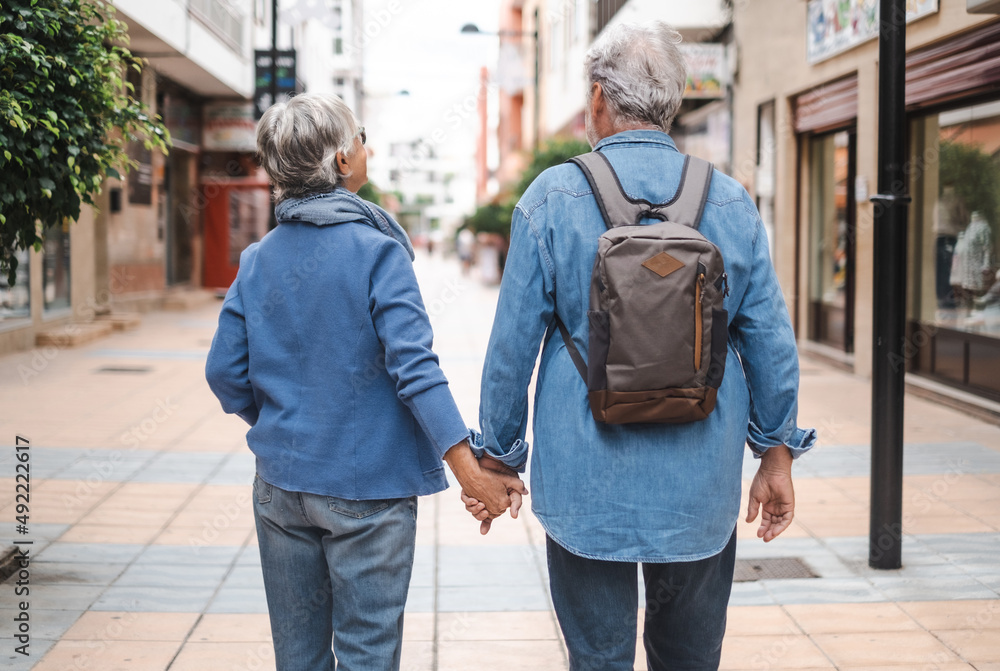 Back view of senior couple of tourist walking in the city. Attractive white haired caucasian people enjoying freedom travel vacation Back view of senior couple of tourist walking in the city. Attractive white haired caucasian people enjoying freedom travel vacation