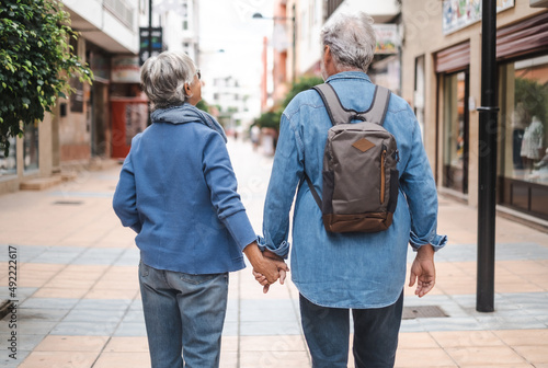 Back view of senior couple of tourist walking in the city. Attractive white haired caucasian people enjoying freedom travel vacation