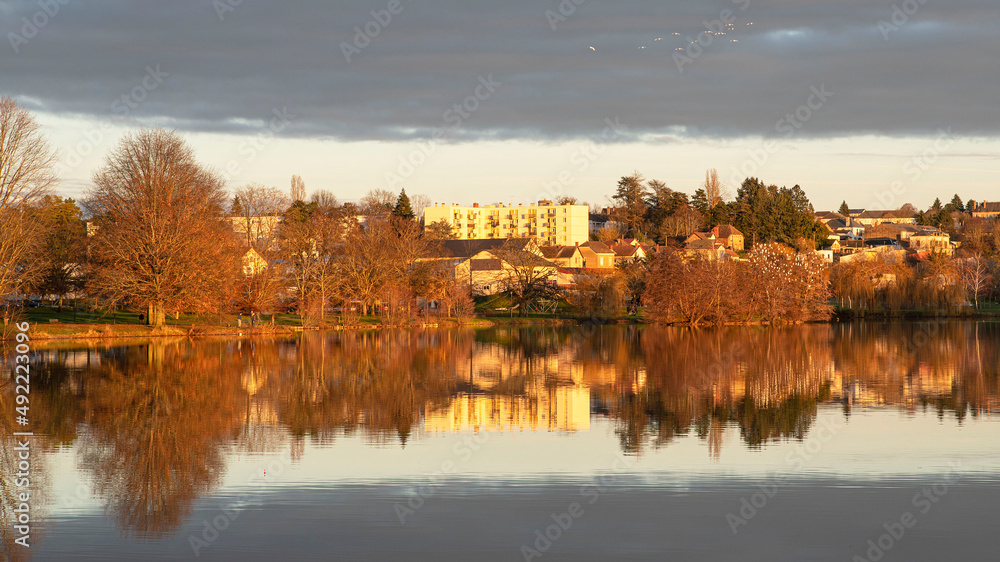 Sunset on a lake in Burgundy, France, with trees in winter and houses and buildings behind