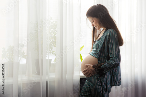 Pregnant girl in pajamas standing by the window