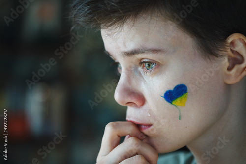Young sad woman with Ukrainian flag symbol on her face crying, stop the war conc Fototapet