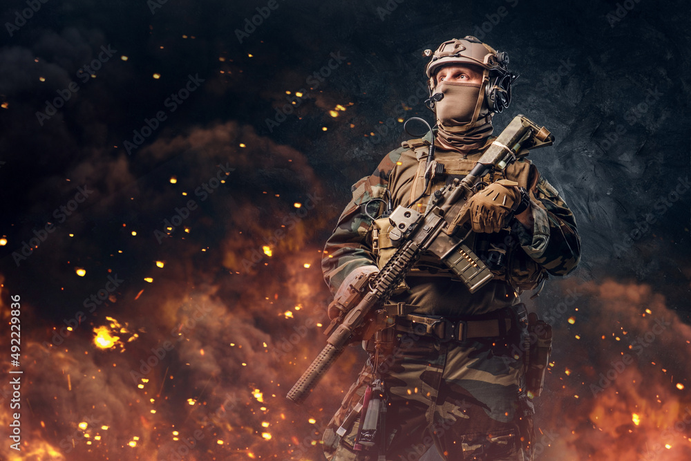 Military soldier dressed in uniform with rifle against flame Military soldier dressed in uniform with rifle against flame
