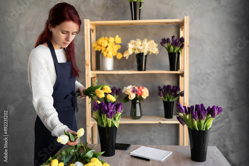 Small business. a woman florist in a flower shop near a showcase with tulips in an apron collects a bouquet of tulip flowers. Flower delivery, ordering.