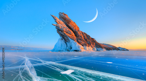 Ogoy island on winter Baikal lake with transparent cracked blue ice at sunrise in the background crescent - Baikal, Siberia, Russia