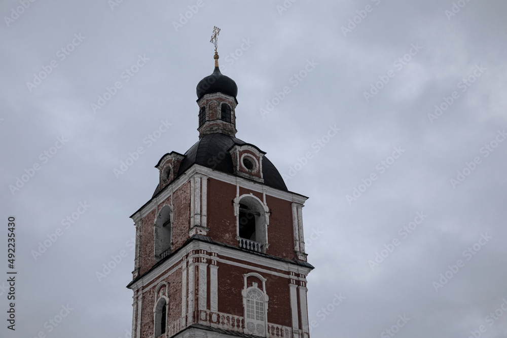 Beautiful tower of an ancient monastery. Stone ancient architecture. Cloudy winter day.