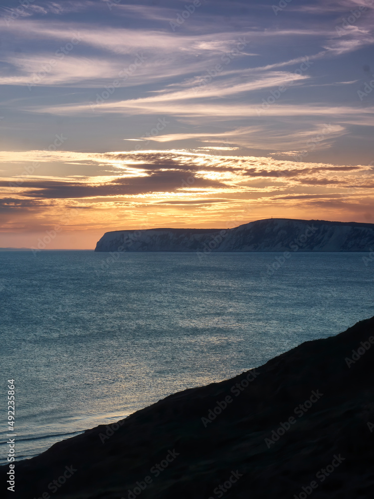 A radiant, glorious sunset over sea and chalk cliff headlands of the Isle of Wight, with the rich golden rays reflected in the textured waters.