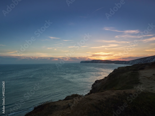 A radiant, glorious sunset over sea and chalk cliff headlands of the Isle of Wight, with the rich golden rays reflected in the textured waters.