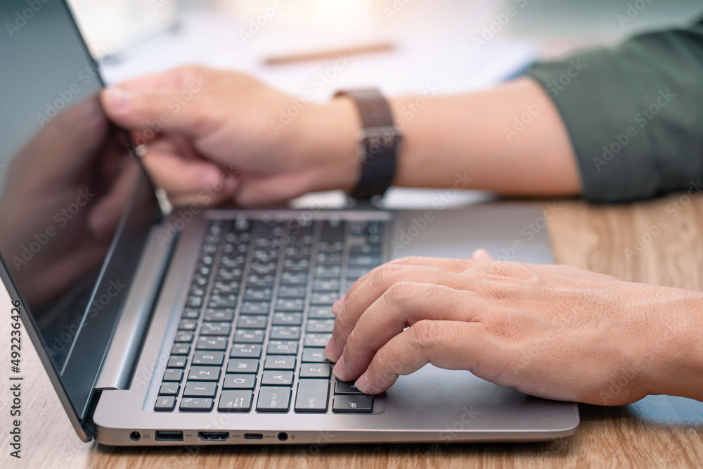 Close up hand a man typing on laptop keyboard on wood deck and document in a blur background business concept Close up hand a man typing on laptop keyboard on wood deck and document in a blur background business concept