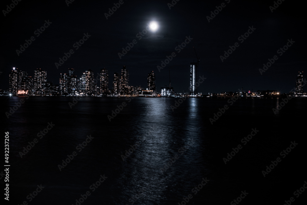 A large bright moon shines over the East River from Queens and reveals a city skyline.