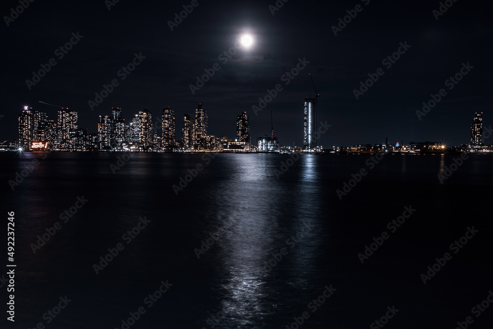 A large bright moon shines over the East River from Queens and reveals a city skyline.