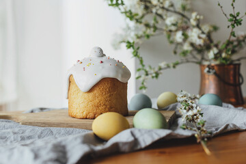 Happy Easter!  Homemade easter bread, natural dyed eggs and spring blossom on rustic table in room. Stylish freshly baked easter cake with sugar glaze and sprinkles, traditional ukrainian bun