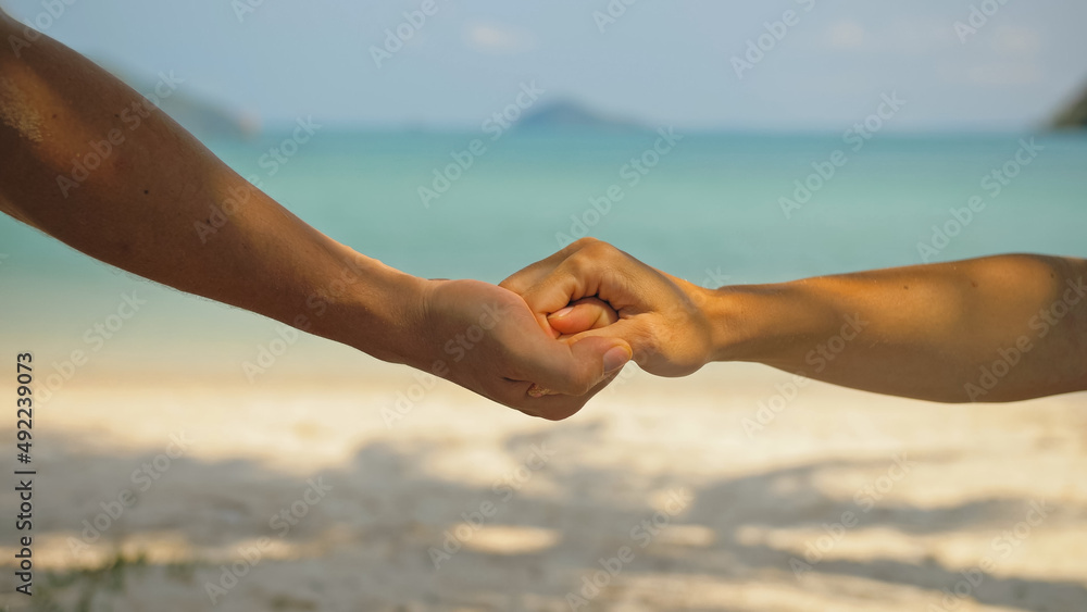 Hands of flirting young man and woman touching on beach in palms shadow against calm azure ocean close view. Traveling to tropical countries Hands of flirting young man and woman touching on beach in palms shadow against calm azure ocean close view. Traveling to tropical countries
