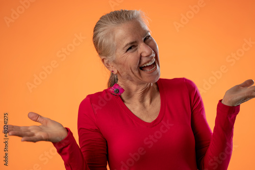 Portrait of pretty mature woman unsure in disbelief, questioning, isolated on solid orange background with copy space.