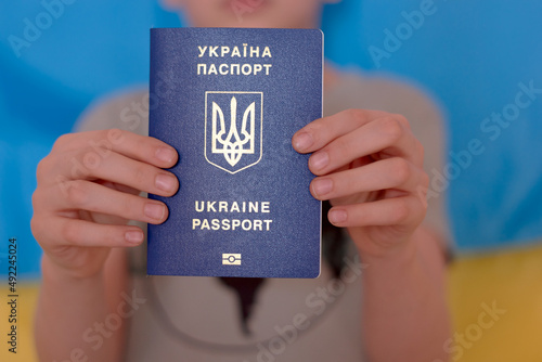 Boy holding in hands Ukrainian passport on yellow-blue flag background. Russian invasion in Ukraine