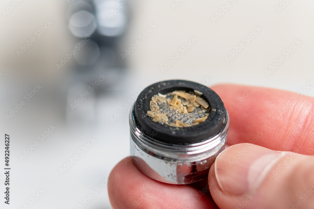 Rust scales in a clogged dirty bathroom faucet aerator closeup in hand