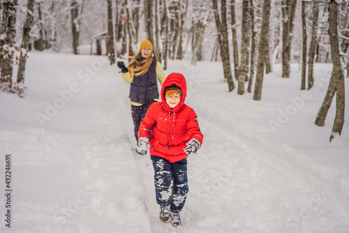 Obraz na płótnie Funny little boy and his mom in blue winter clothes walks during a snowfall. Outdoors winter activities for kids. Cute child wearing a warm hat low over his eyes catching snowflakes with his tongue w salonie