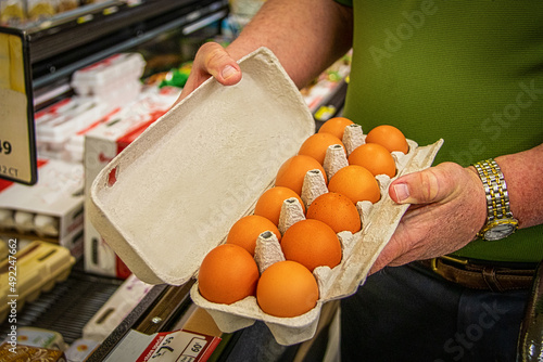 Man checking carton of brown eggs at supermarket for cracked eggs before he purchases them
