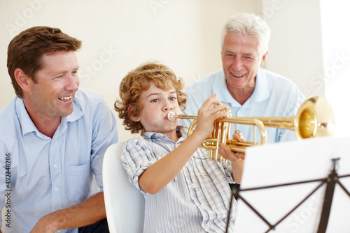 Musical talent runs in this family. Shot of a cute little boy playing the trumpet while his father and grandfather watch him proudly.