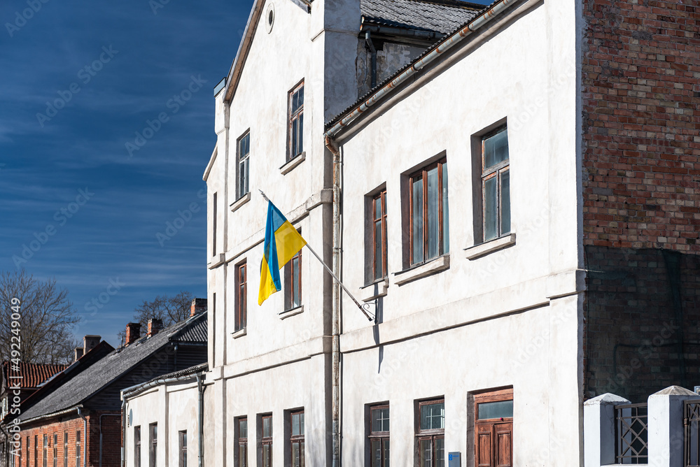Fototapeta premium An old house with the Ukrainian flag. National flag of Ukraine waving in the wind in sunny day.