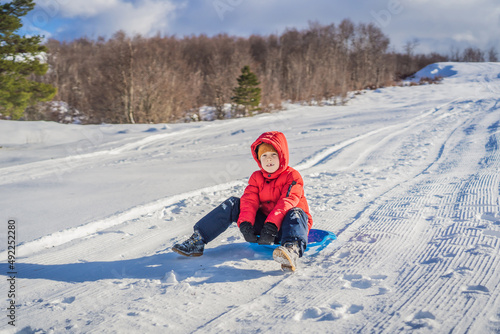 happy and positive little boy enjoying sledding and cold weather outdoor, winter fun activity concept