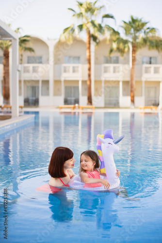 Family look, swimwear outfit. Beautiful mother with her pretty daughter with an inflatable ring in the form of a unicorn having fun and relaxed on swimming pool on villa beach. Summer time vacations © sofiko14