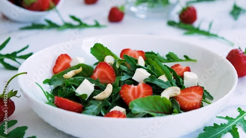 Vitamin salad of strawberry with arugula, spinach leaves, feta cheese and cashew nuts with salad leaves and fresh strawberry fruits around. Vegan food, keto diet and paleo diet. 4K, camera movement.