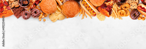 Junk food top border over a white marble banner background. Selection of take out and fast foods. Pizza, hamburgers, french fries, chips, hot dogs, sweets. Top down view with copy space.
