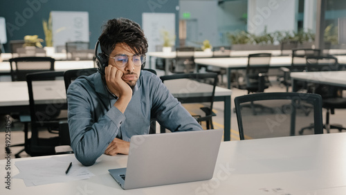 Bored man Arabian man Indian service manager in headphones have displeased look video conference webinar learn language improve self-education professional skills studying with difficult task boredom