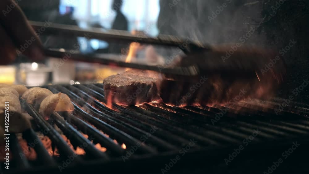 Roasting juicy meat steak with spices and herbs in burning charcoals fire on bbq grid, flames and smoke in slow motion. Juicy steak with grilling stripes ready for picnic celebration. Barbecue grill