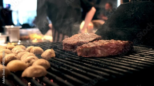 Roasting juicy meat steak with spices and herbs in burning charcoals fire on bbq grid, flames and smoke in slow motion. Juicy steak with grilling stripes ready for picnic celebration. Barbecue grill