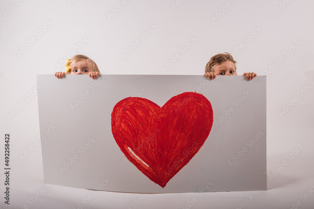 Boy and girl are holding white board with big heart on white background ...