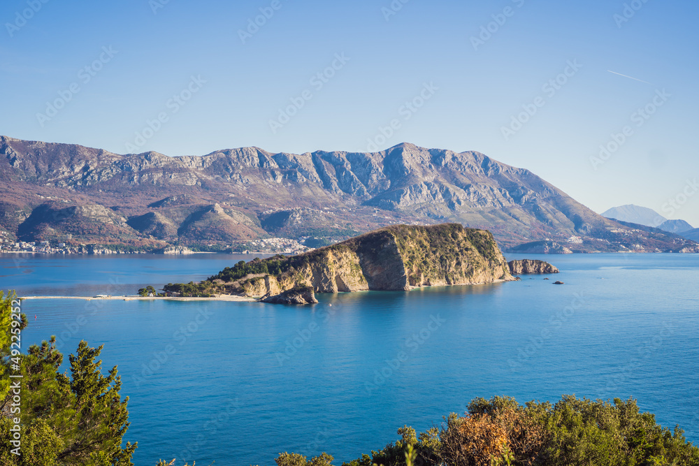 Fototapeta premium Aerial view of Sveti Nikola, Budva island, Montenegro. Hawaii beach, umbrellas and bathers and crystal clear waters. Jagged coasts with sheer cliffs overlooking the transparent sea. Wild nature