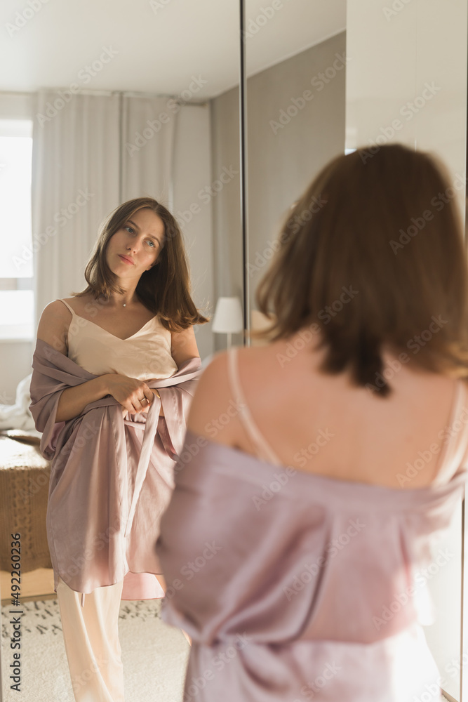 Fototapeta premium Happy morning. Attractive young woman looking in mirror at her apartment