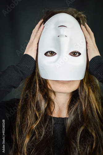 Being different even when wearing a mask - portrait of a young long-haired woman with a mask upside down and hands on her head - concept