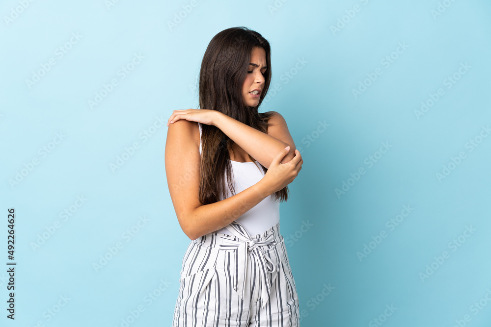 Young brazilian woman isolated on blue background with pain in elbow Young brazilian woman isolated on blue background with pain in elbow